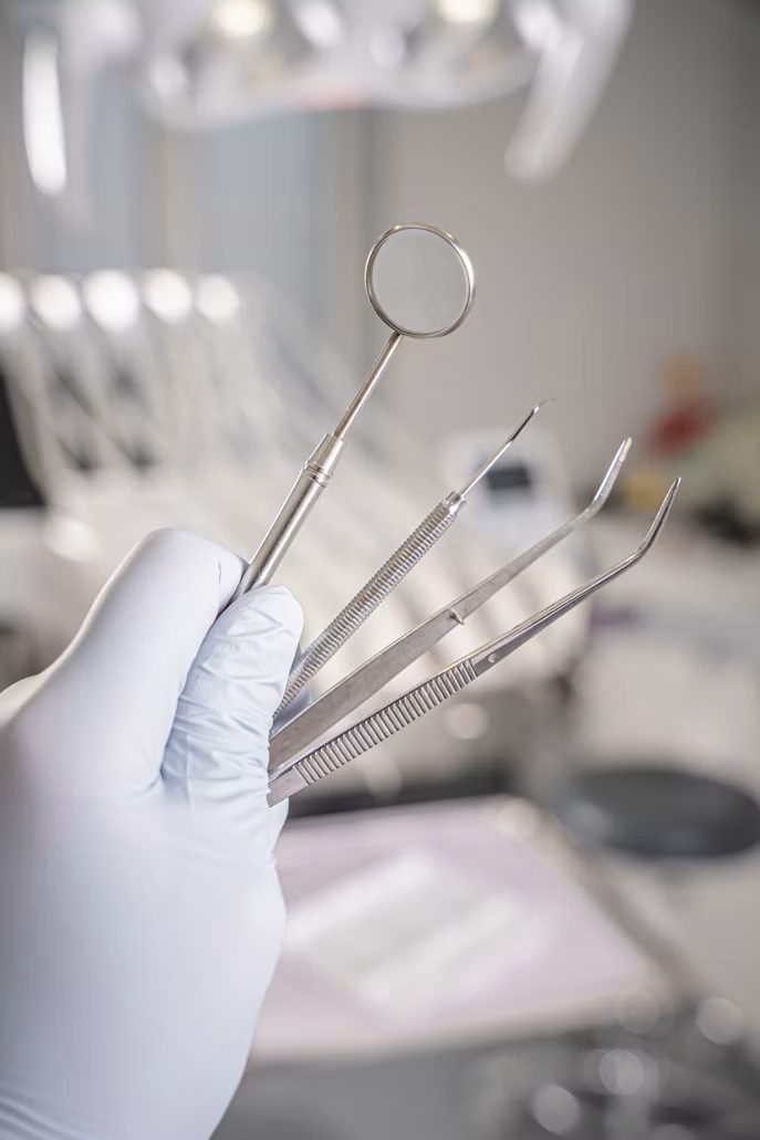 Une main gantée tient miroir, sonde et précelles prêts à l’emploi